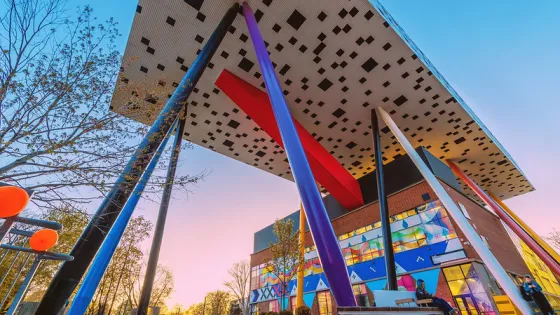 Photo of the Rosalie Sharp Centre for Design building, a tabletop building on stilts, with blue sky and the side view of the building with a mural