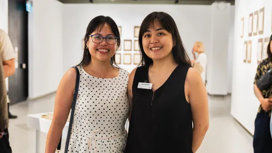 Two women side by side in an art gallery.