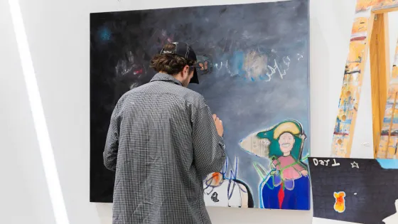 An artist doing final touches to a large abstract painting hanging on the wall