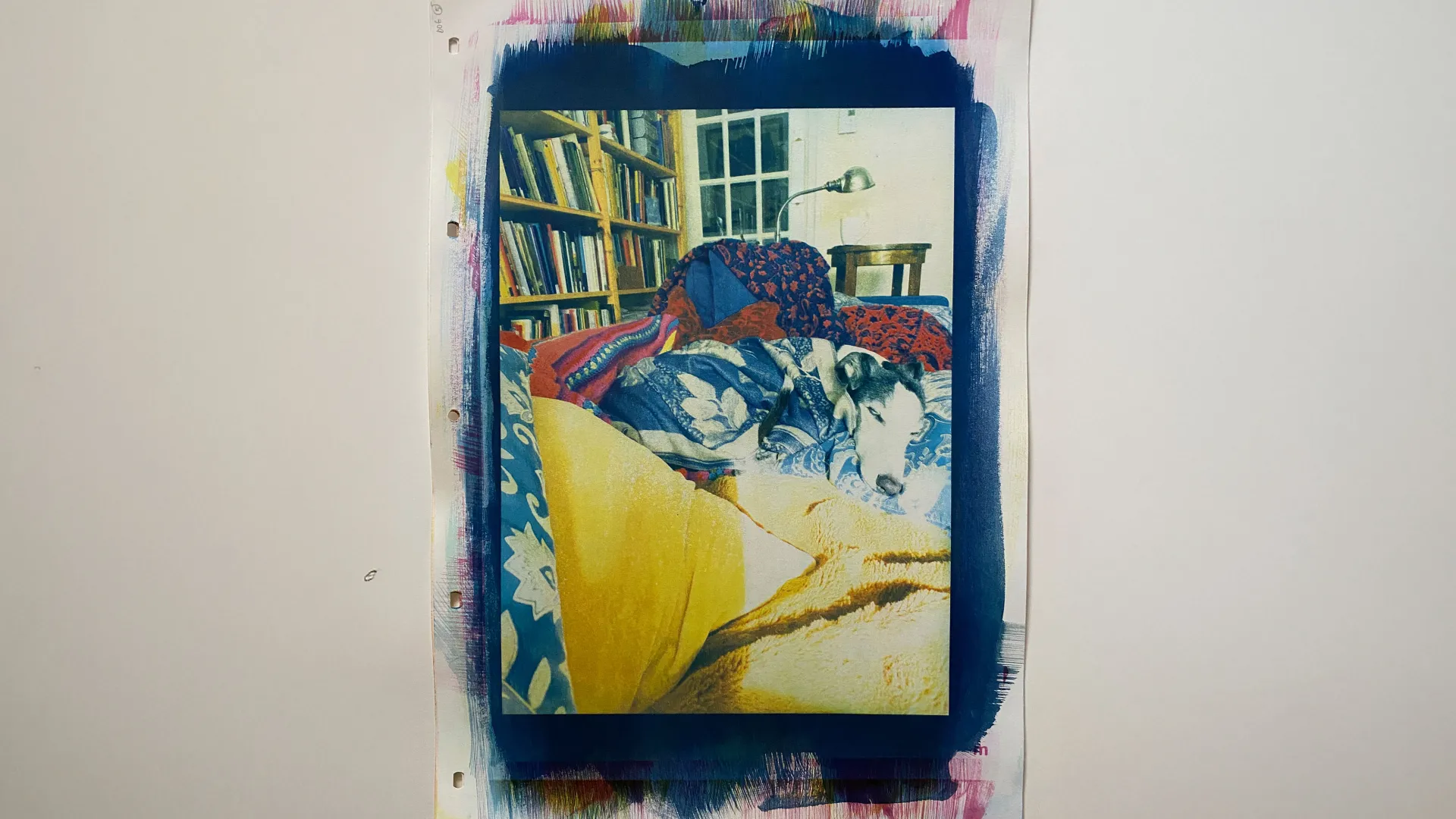 this is a colour print with a portrait orientation \ a black & white dog \ S \ a whippet is centred \ laying on a couch snuggled in blankets & pillows \ in the background there is a bookcase \ a light \ and a cup of tea to the right of the print is a handwritten poem \ which could be understood as the beginnings of an escape into drawing