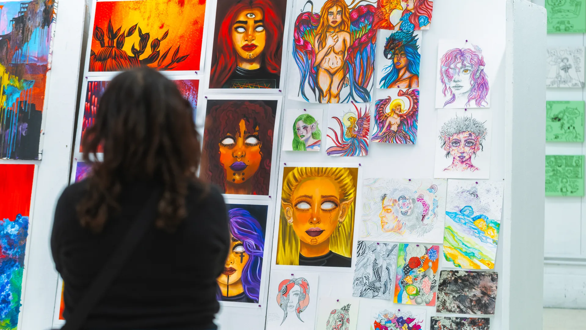 Person standing at a gallery wall covered in small paintings