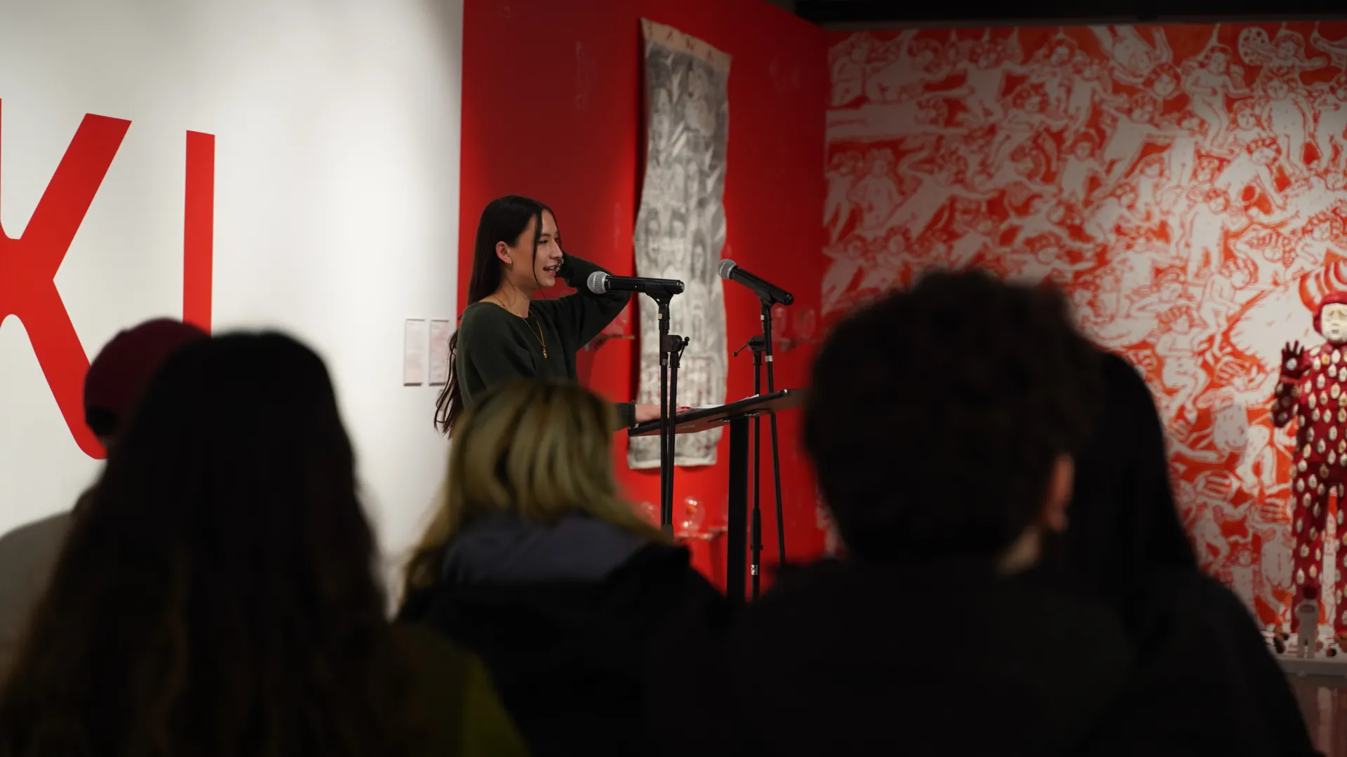 An image a woman with long black hair and long sleeve shirt talking an audience