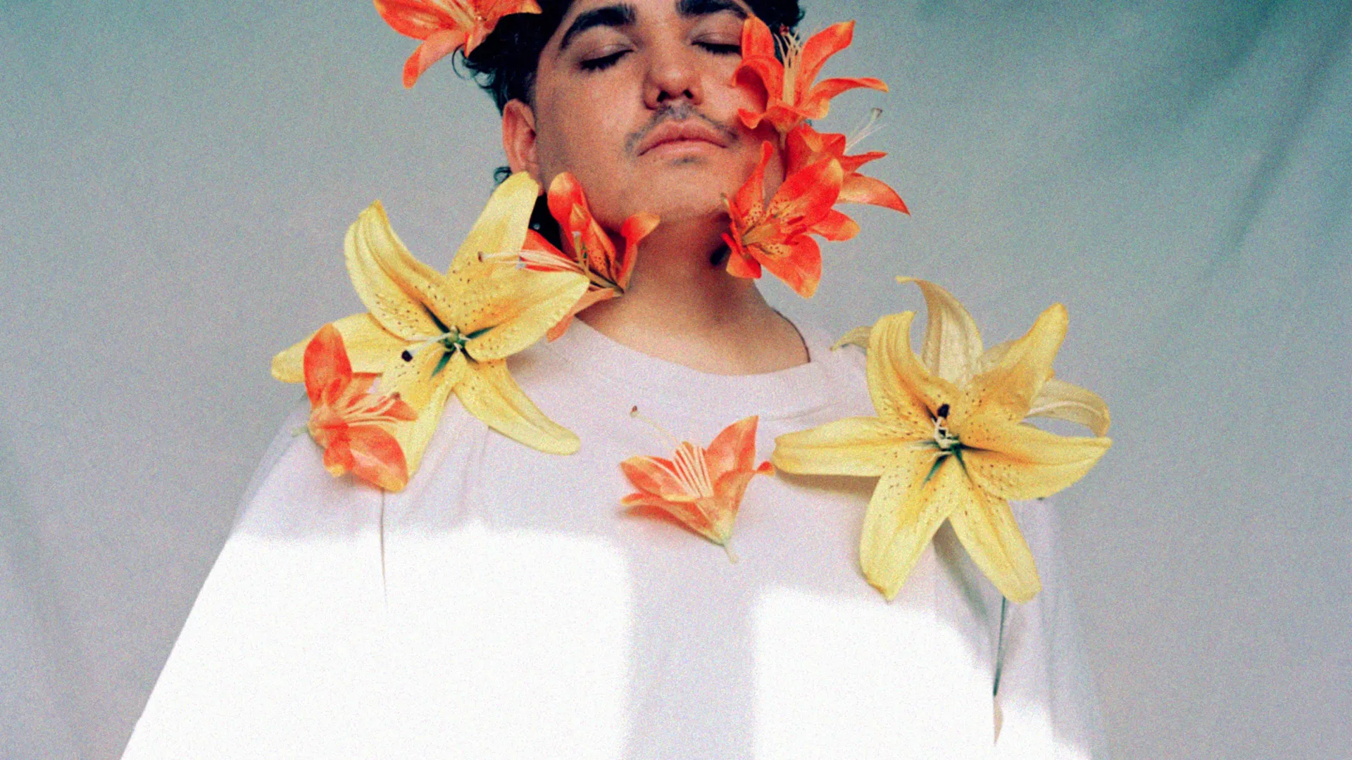 A man with black short hair wearing a white t-shirt with yellow and orange lilies on them