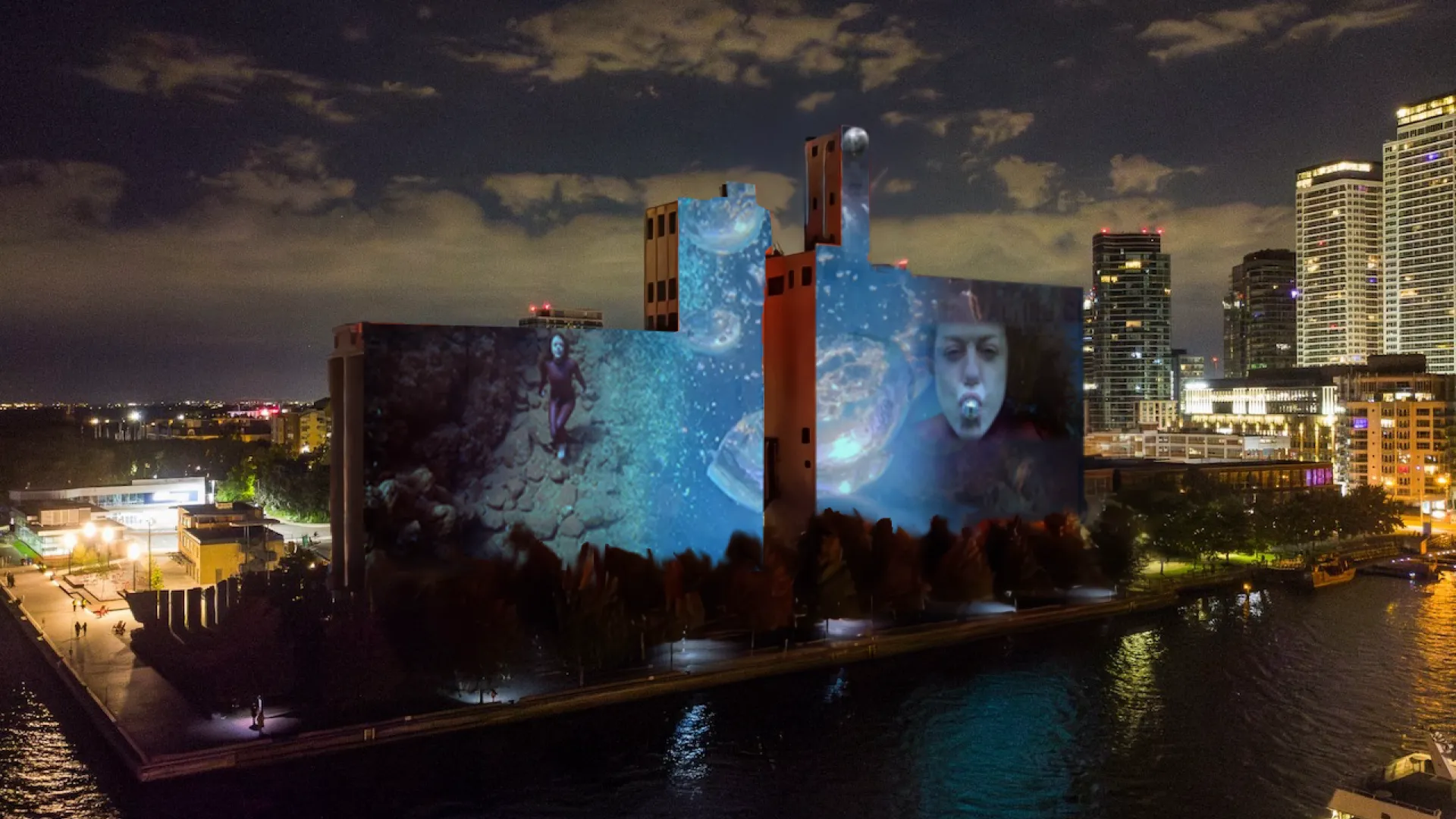 Artwork projected, Melting Temporalities on Canada Malting Silos, woman swimming at left, face of woman with a silver ball in her mouth
