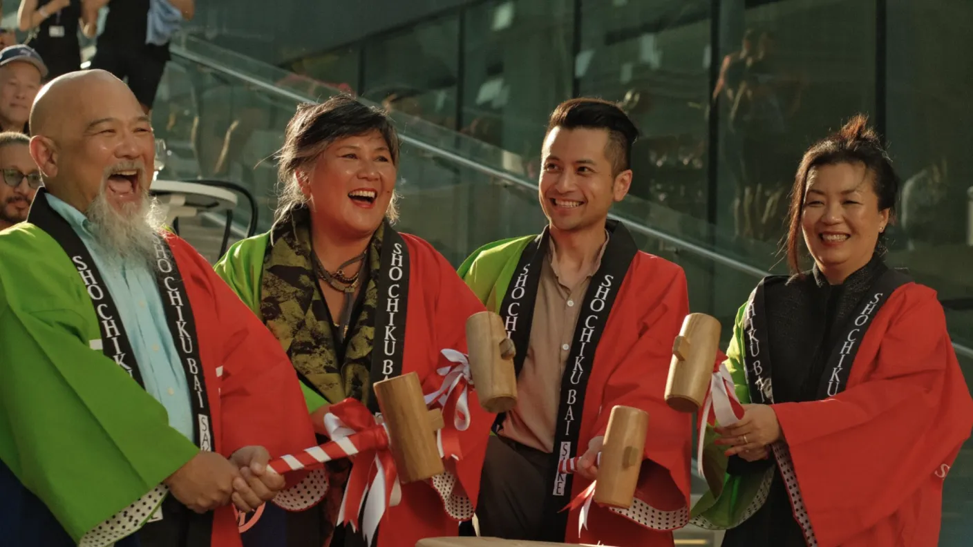 Four people in cultural adornment holding mallets over a drum.