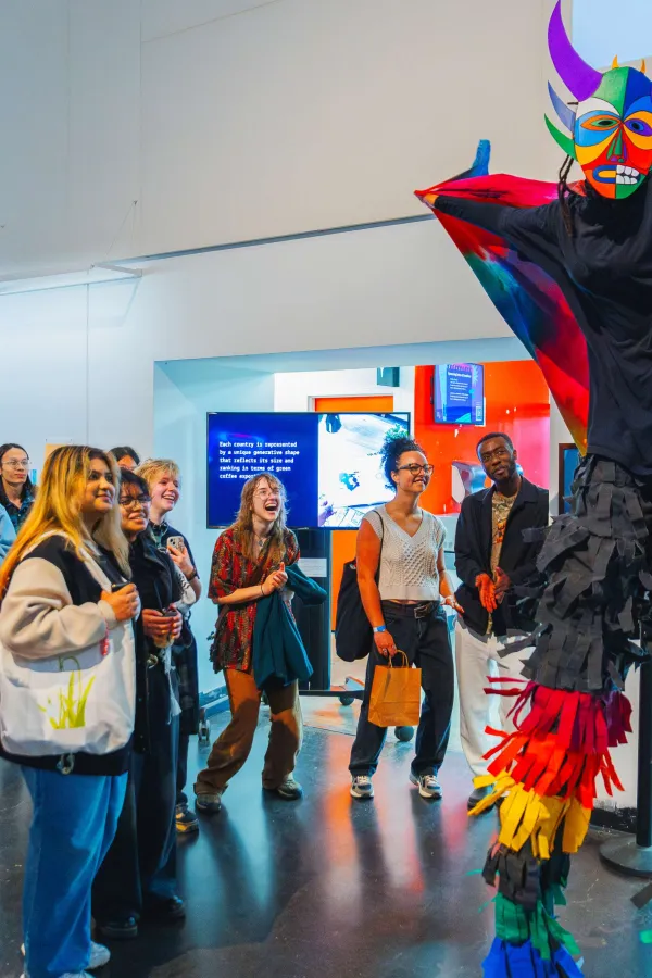 Person on stilts in colourful clothing performing in front of a small group
