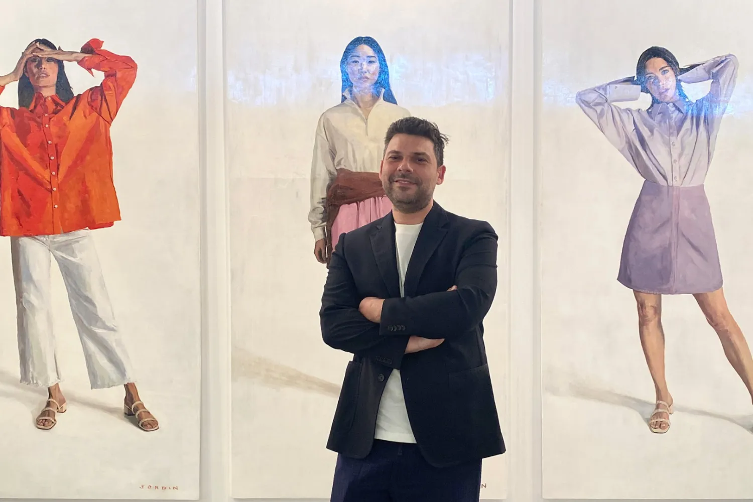 A man standing in front of three large paintings of stylish women.  