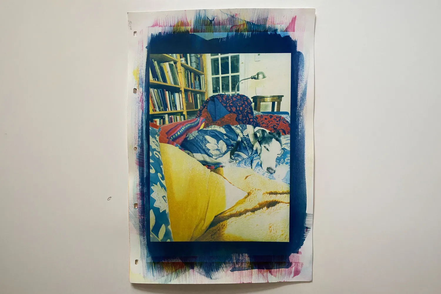 this is a colour print with a portrait orientation \ a black & white dog \ S \ a whippet is centred \ laying on a couch snuggled in blankets & pillows \ in the background there is a bookcase \ a light \ and a cup of tea to the right of the print is a handwritten poem \ which could be understood as the beginnings of an escape into drawing