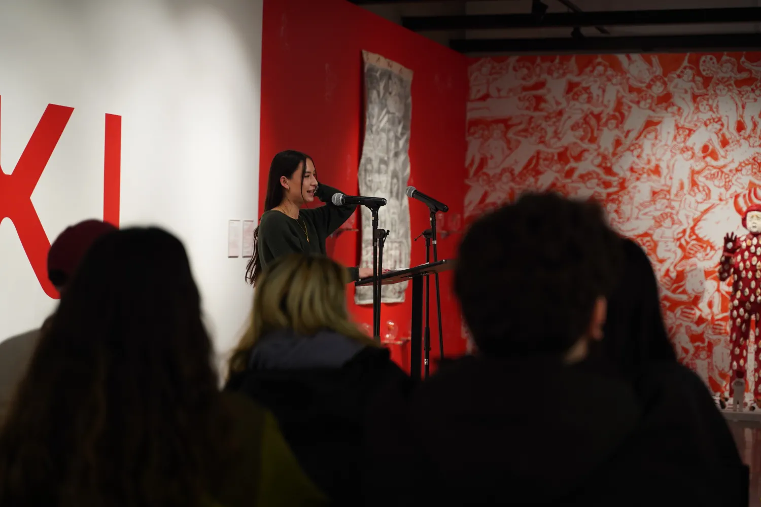 An image a woman with long black hair and long sleeve shirt talking an audience