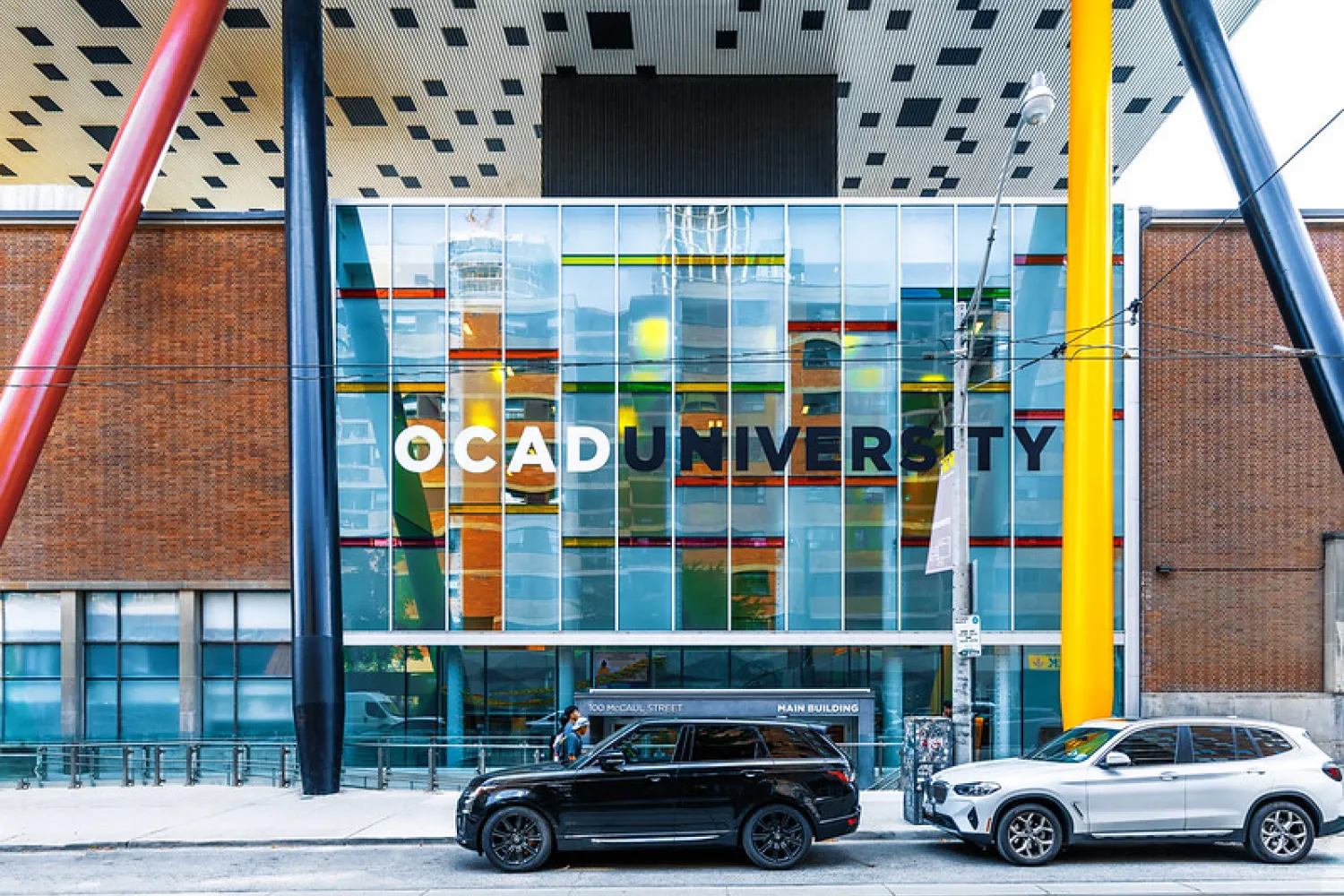 Colour photo of OCAD University front entrance with two cars (black and white) in the foreground on the street.