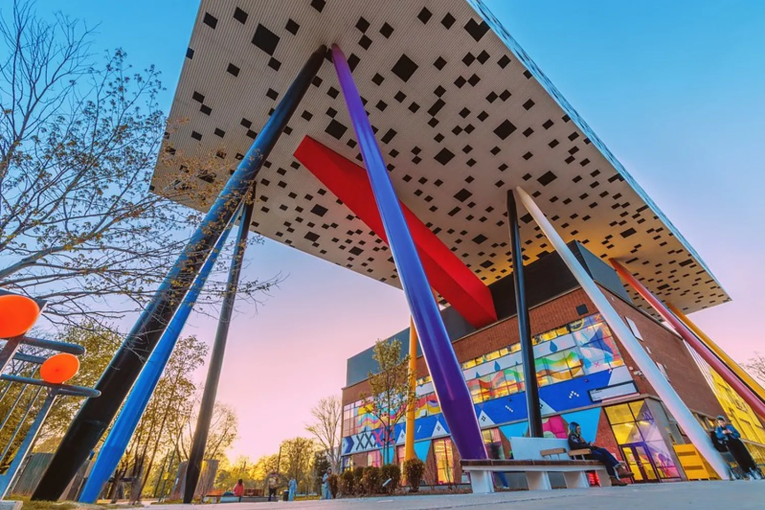 Colour photo of OCAD University from low angle, showing pillars of various colours beneath a roof that is white with black scattered squares. 