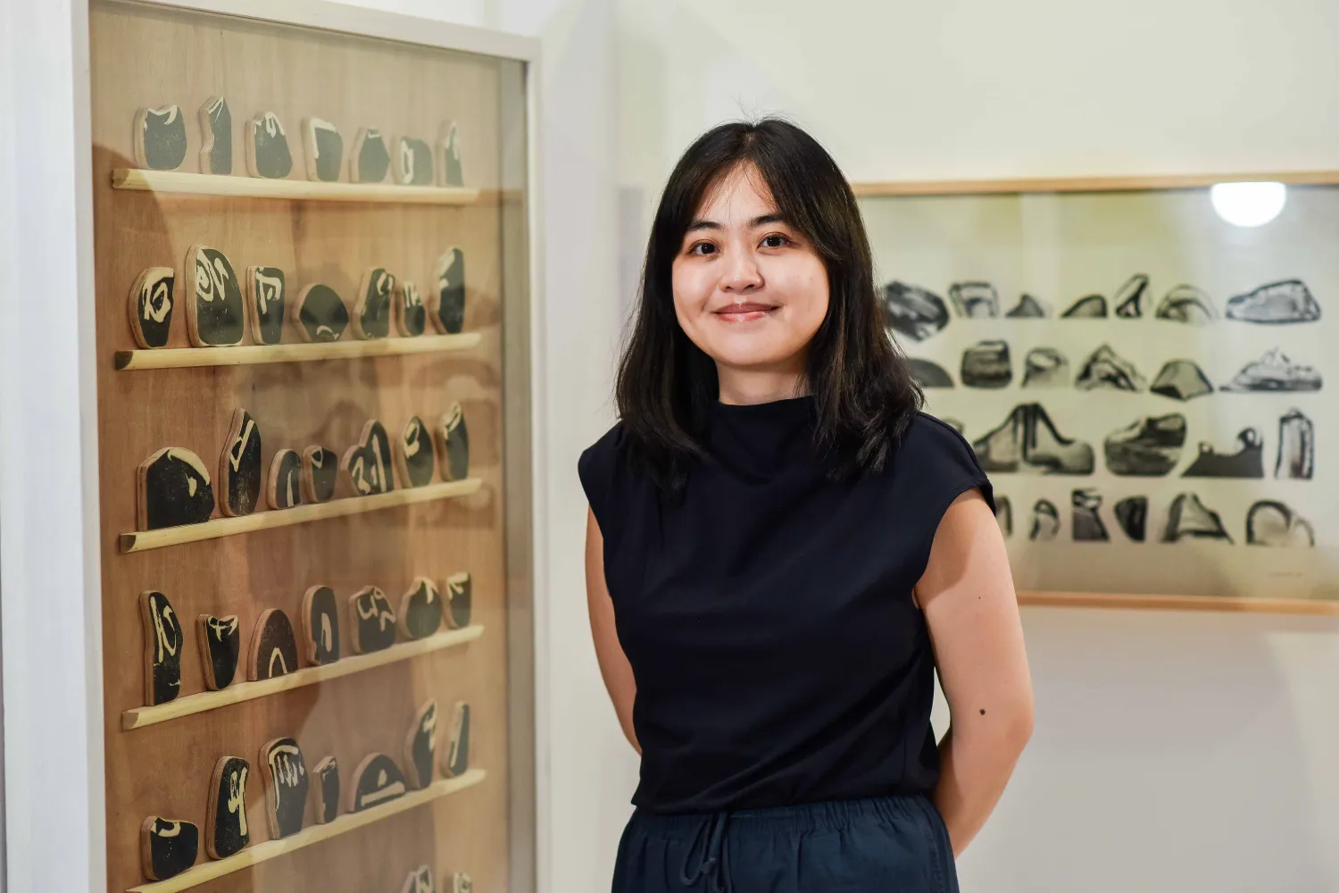 Photo of woman with dark hair, dressed in black, smiling in front of her artwork