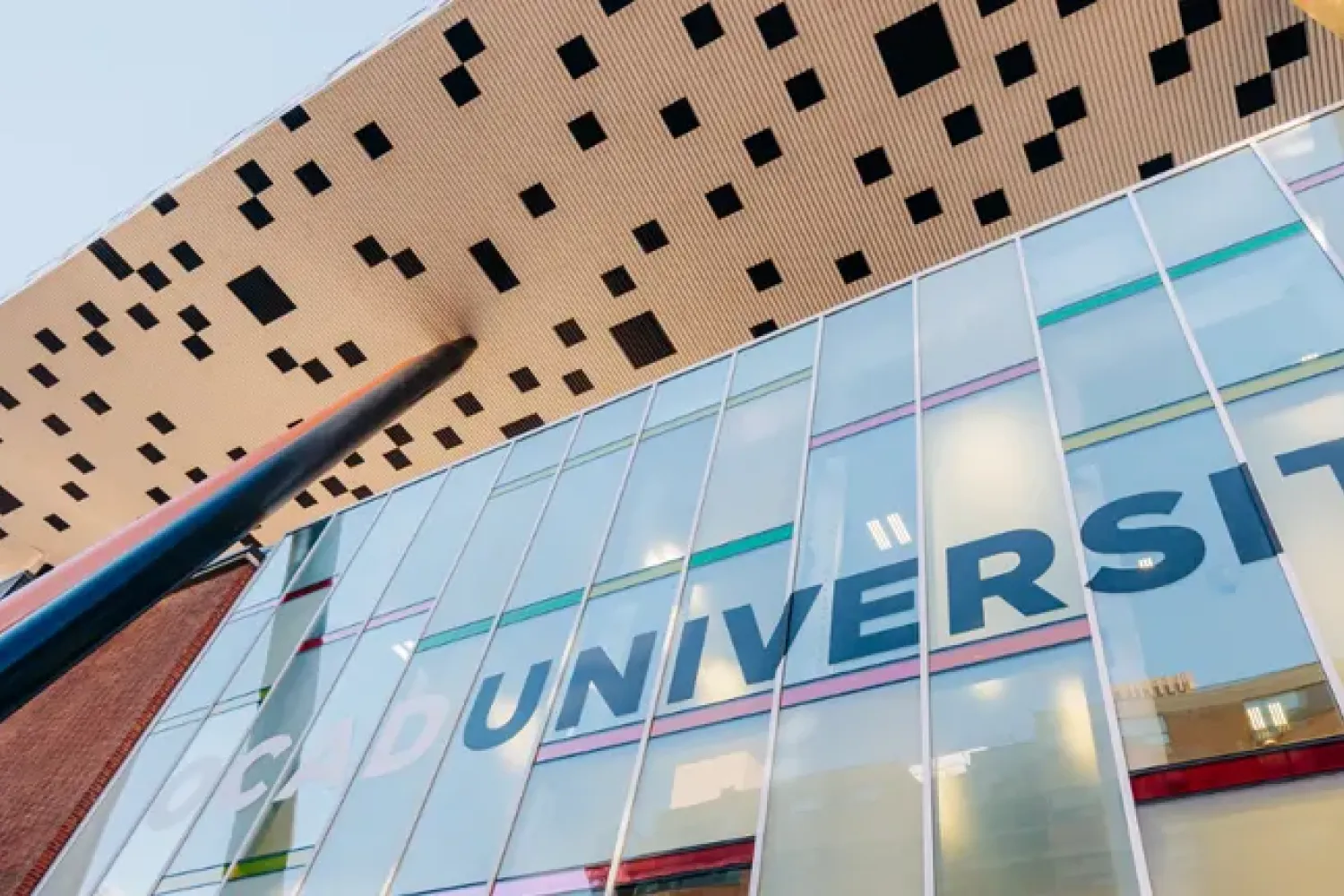 A view of the 100 McCaul St. looking upward, words OCAD University are on the window with the tabletop building on top