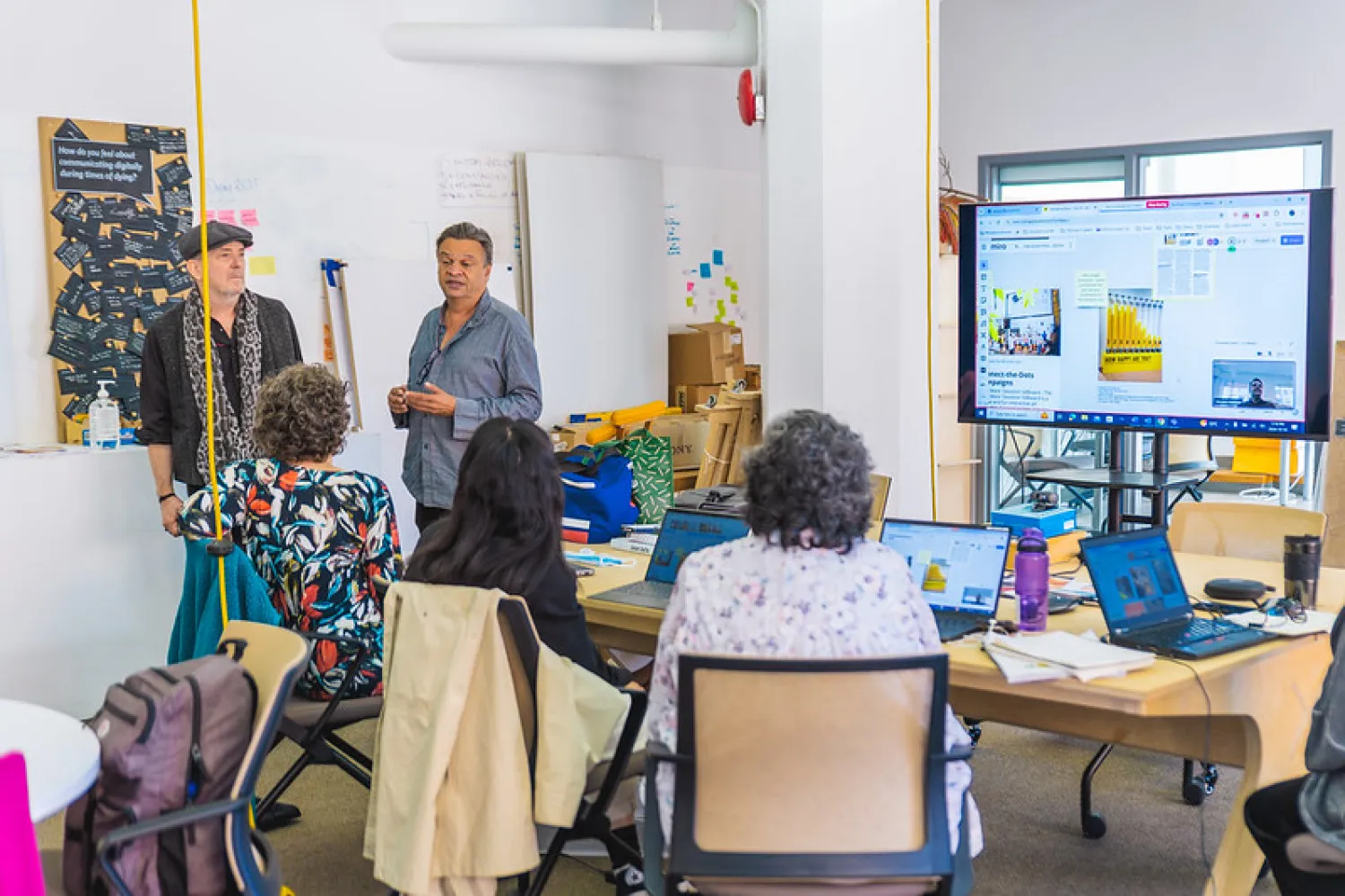 People in a research lab attending a presentation led by two faculty members.