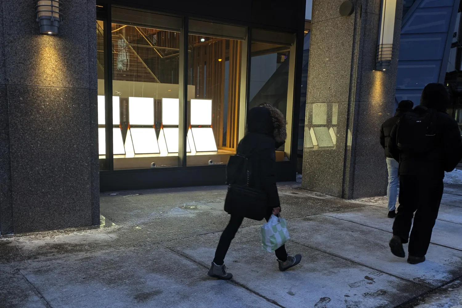 People walking on sidewalk beside light installation in window.