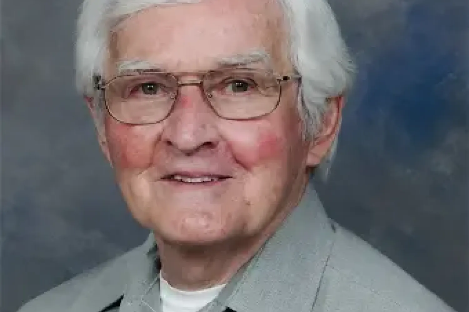 Photo of a man with glasses and white hair wearing a grey shirt with a white t-shirt underneath