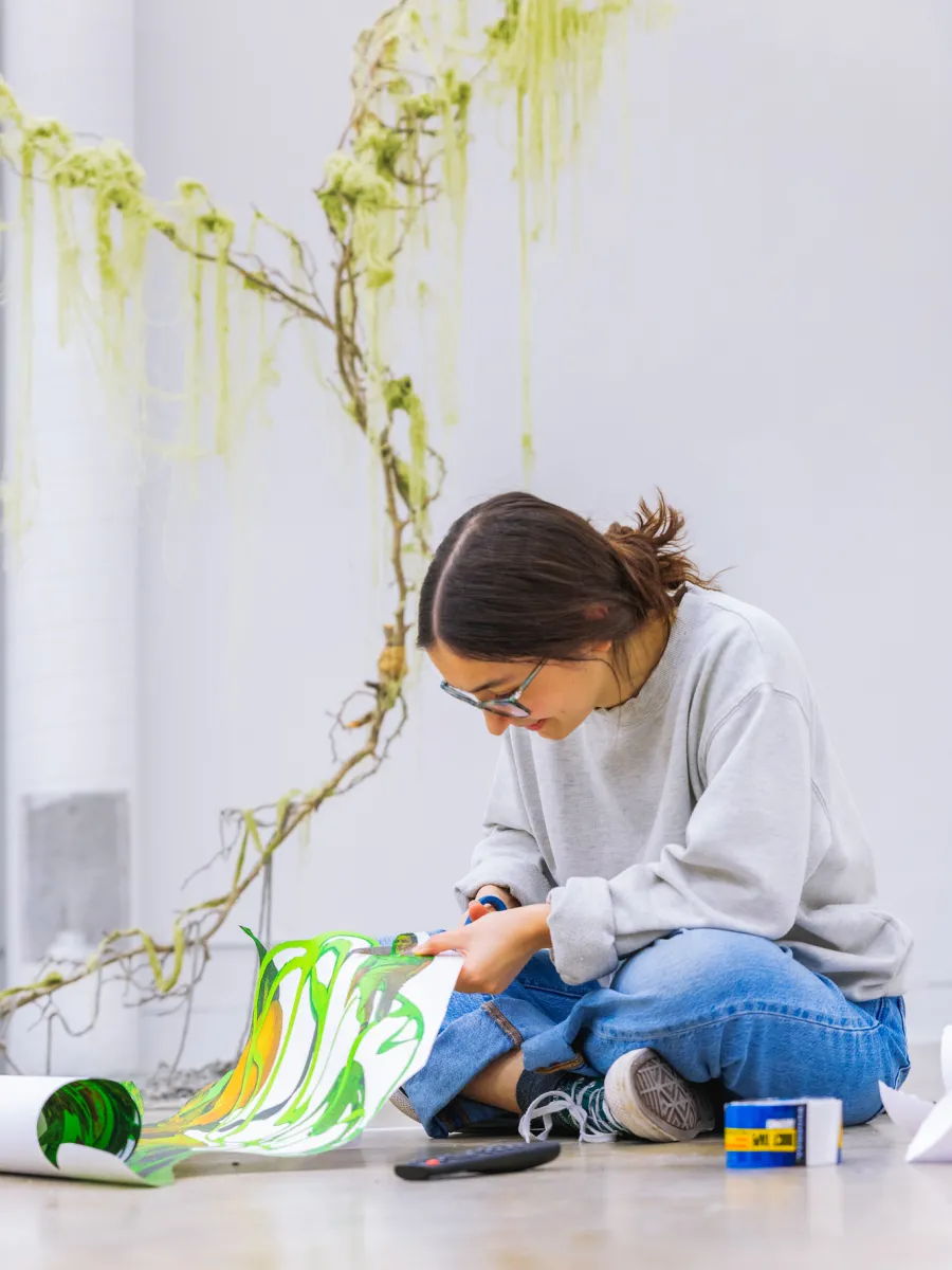 A student sitting on the floor painting with green paint.