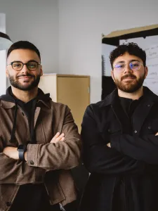 Award-winners Arian Shariaty (left) and Eli Saghbini (right) standing together in a meeting room. 