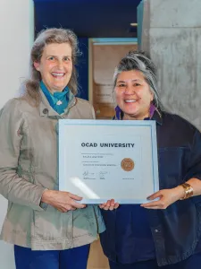 Ana Serrano and Sylvia Whitton stand holding a framed certificate.