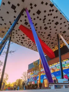 Colour photo of OCAD University from low angle, showing pillars of various colours beneath a roof that is white with black scattered squares. 