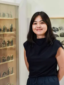 Photo of woman with dark hair, dressed in black, smiling in front of her artwork