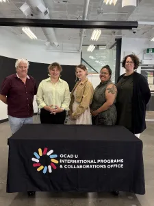 Image (left to right): Dr. David Griffin, Jennie Suddick, Meichen Waxer, Danielle Nadine Pierre and Deanne Fisher standing behind a table with a black tablecloth. The logo on the tablecloth says, "OCAD U International Programs & Collaborations Office."