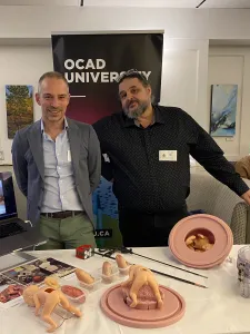 Dr. Tim Van Mieghem and Professor Francis LeBouthillier, standing in front of a table displaying medical surgical models, with an OCAD U banner in the background. 