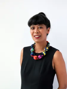 A woman with black hair in a bun wearing sleeves black shirt and colourful necklace