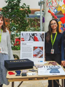 Students standing next to display table of their product design. 