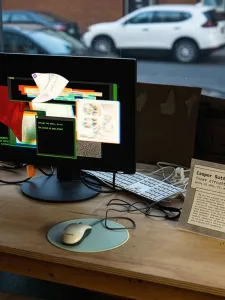 A work desk with a monitor sitting in front of a street facing window.