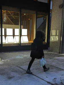 People walking on sidewalk beside light installation in window.