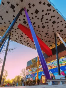 Photo of the Rosalie Sharp Centre for Design building, a tabletop building on stilts, with blue sky and the side view of the building with a mural