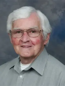 Photo of a man with glasses and white hair wearing a grey shirt with a white t-shirt underneath
