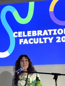 Provost Dr. Sandra Gabriele standing at podium with microphone, background slide of blue with colourful swirl saying, Celebration of Faculty 2026