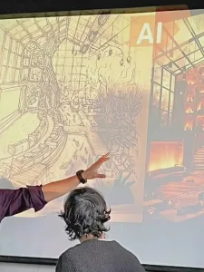 Photo of man at left with glasses pointing to a screen with two graphics