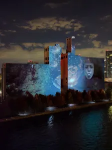 Artwork projected, Melting Temporalities on Canada Malting Silos, woman swimming at left, face of woman with a silver ball in her mouth