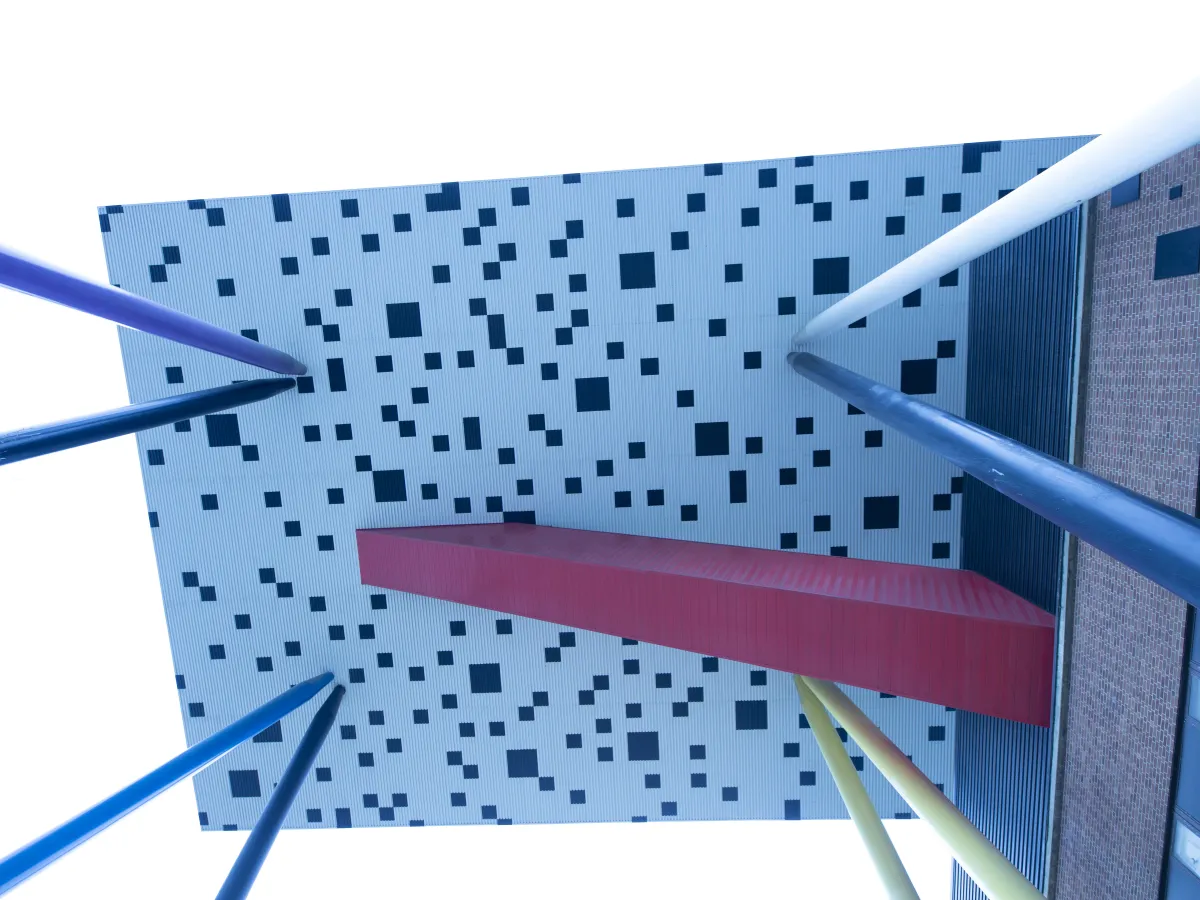 View from below of white building with black checkers on colourful stilts.