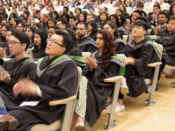 Students in graduation robes, sitting in an auditorium.
