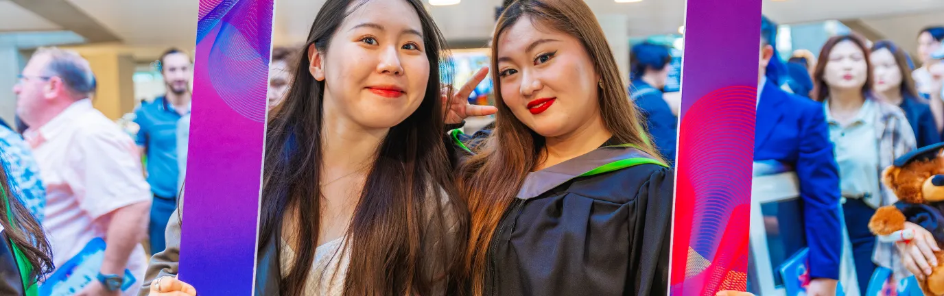 Two students, one in graduation robes posing in a frame.