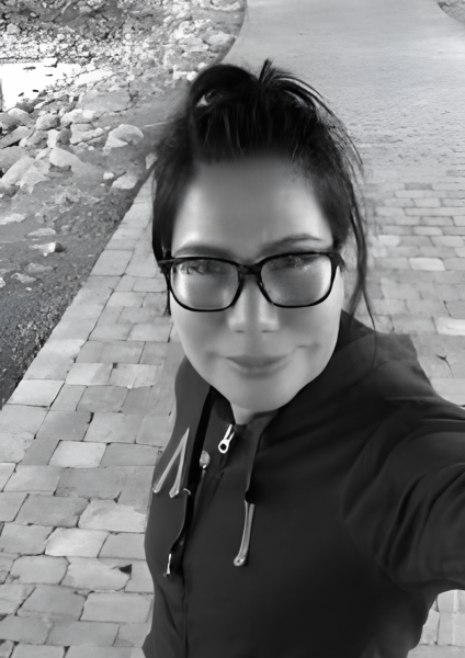 Black and white image of a woman with tied black hair and wearing eye glasses with black jacket