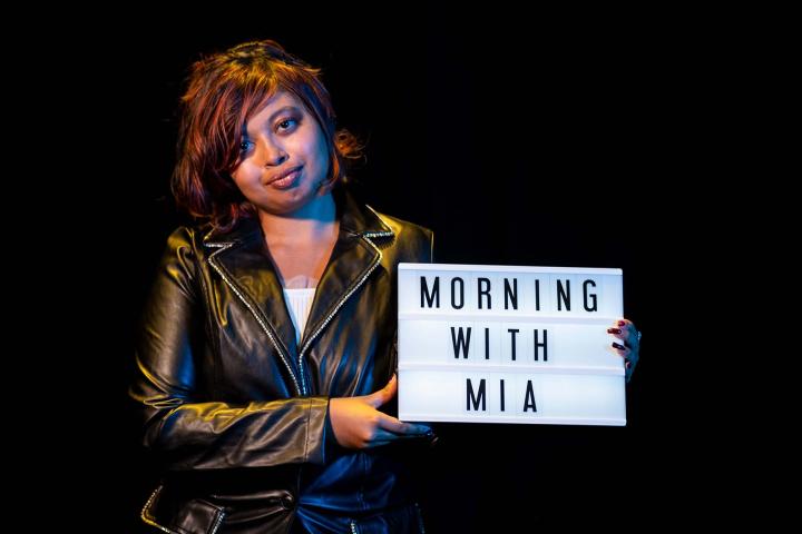 A photo of a young woman holding a sign that reads Morning With Mia