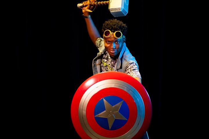 A photo of a young man with a captain America shield and Thor hammer.