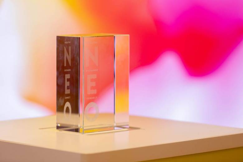 Image of glass block with NEO engraved against orange and pink background.