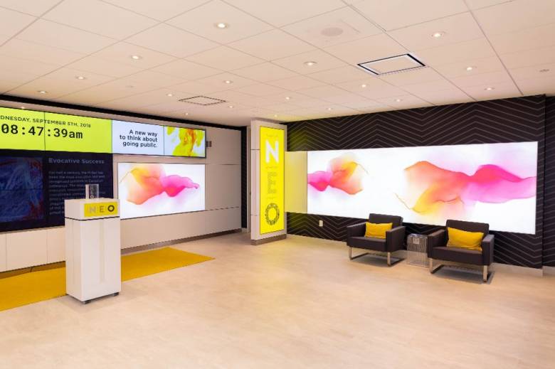 Image of Neo Exchange lobby with tv screens and podium in pink and yellow