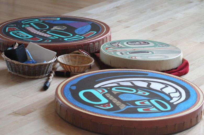 A photograph of three blue and turquoise Haida drums laid out on a wood floor. 