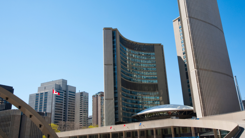 A photo of Toronto’s City Hall on a cloudless day with a Canadian flag on the left of the image.