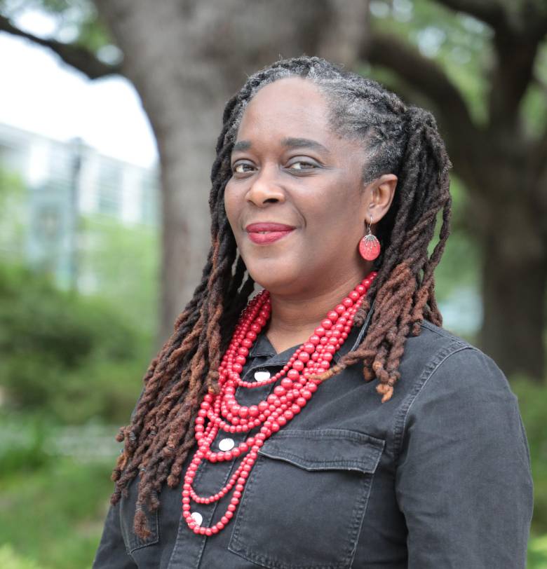 Black woman with long black/brown hair wearing a red necklance and black blouse