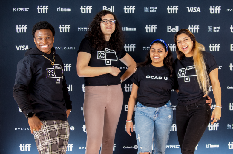 A photo of four students who are OCAD U LiVE content creators wearing black t-shirts with OCAD U branded with the background banner with words, tiff, Toronto, Bell, VISA. 
