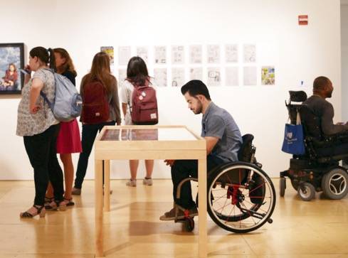 A wheelchair user enjoys an exhibit with displays presented at a table height
