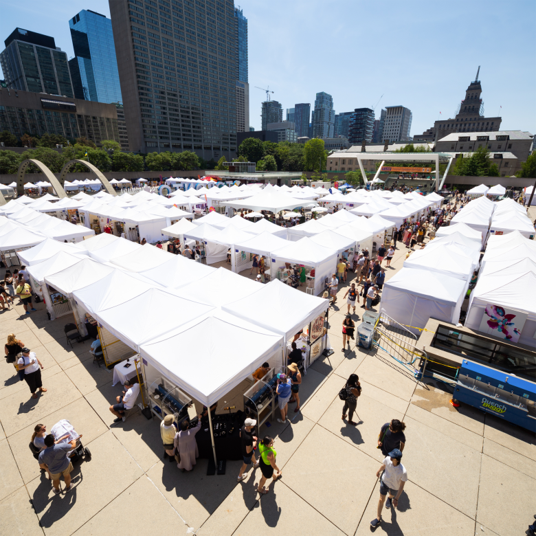 Photo of the tops of many white tents set up across Nathan Philips Square in the summer, with people walking around throughout.